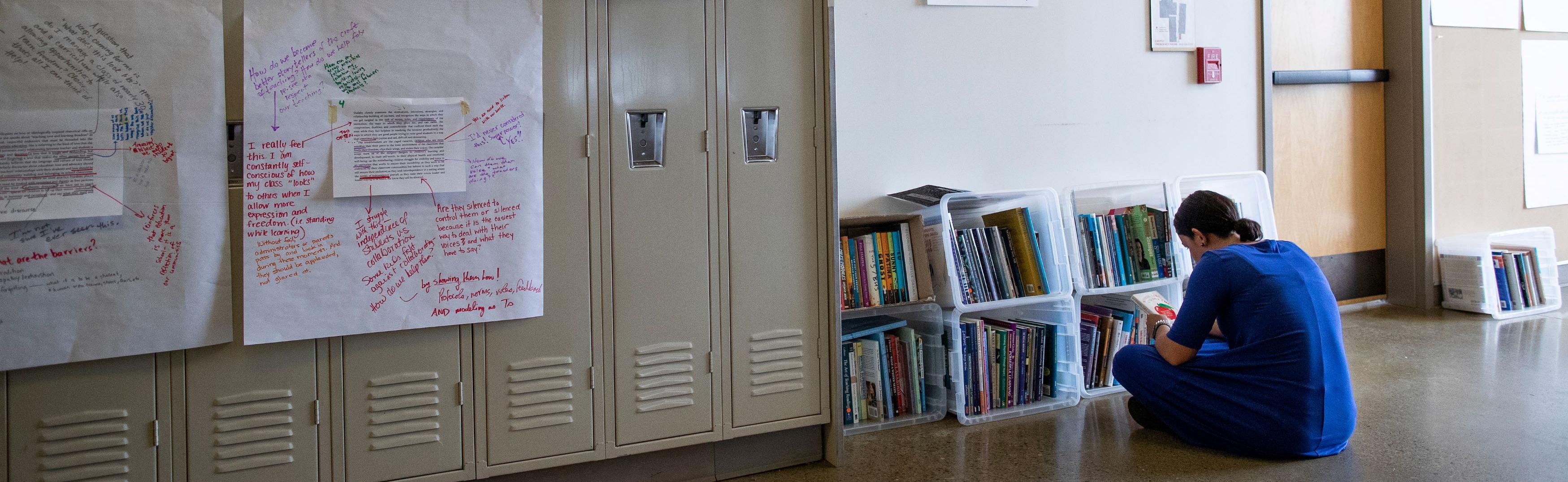 Woman sits by book shelf in hallway and reads book